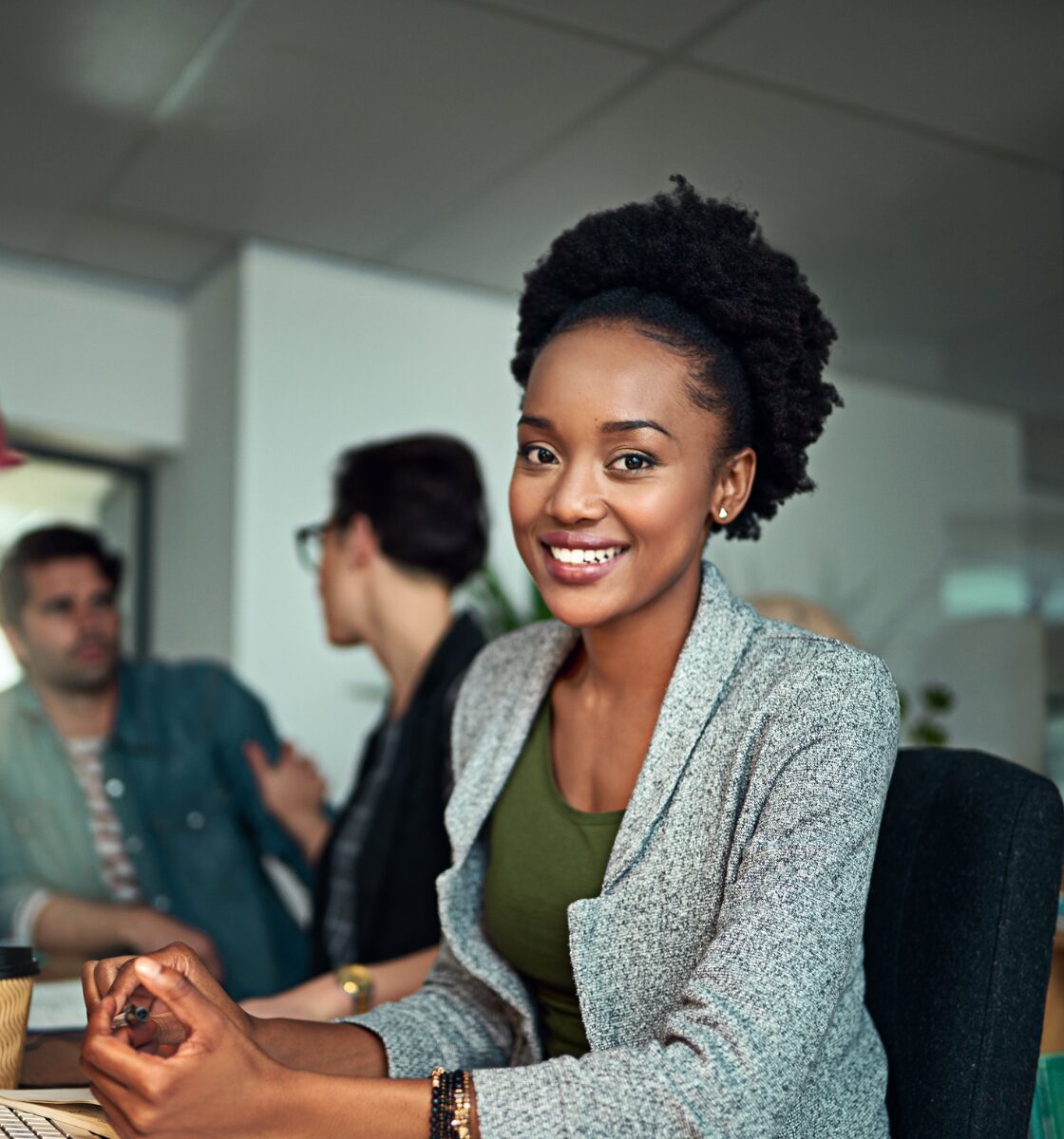 Woman smiling and facing the camera in an office with two men talking in the background
