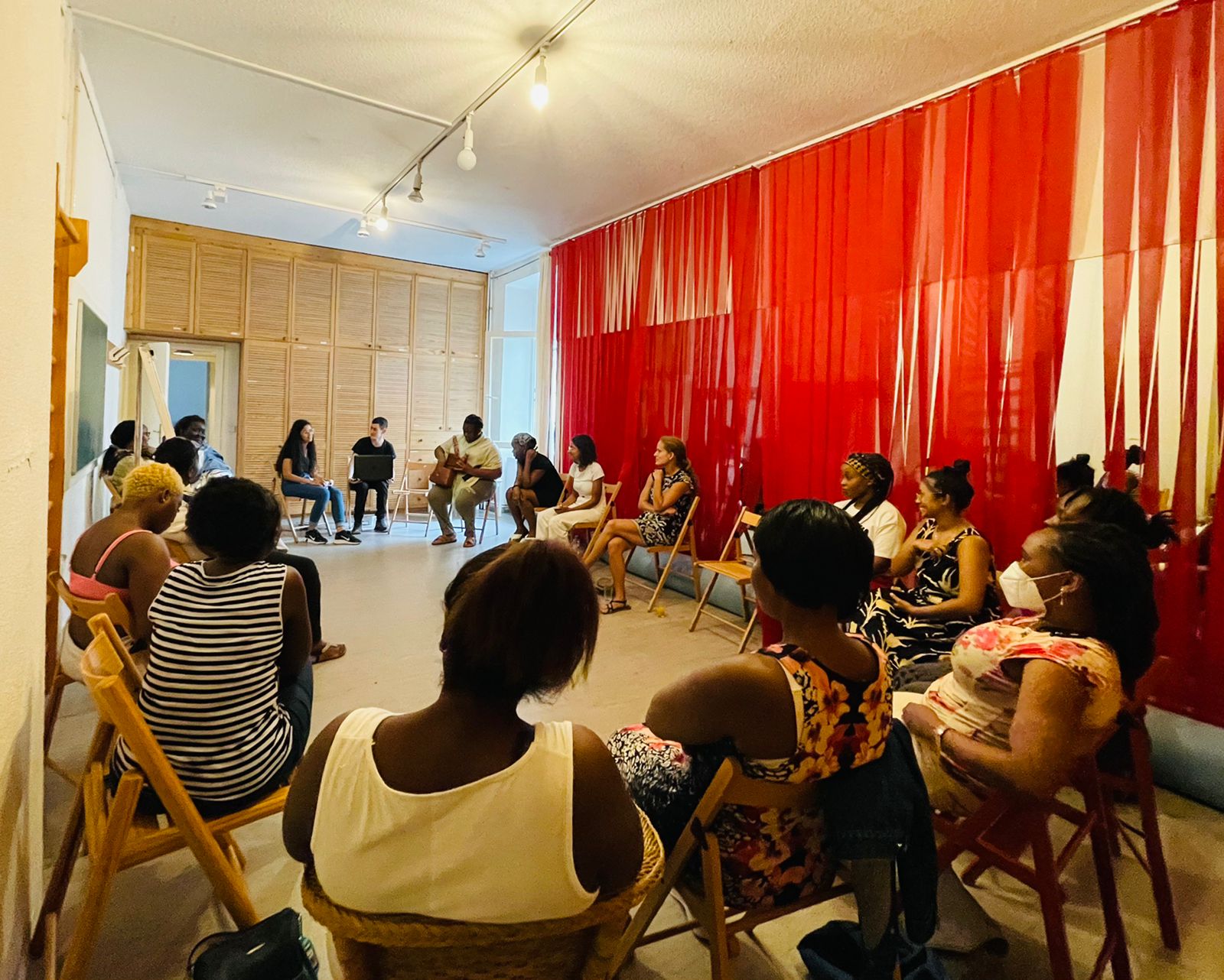 Group of people sitting in circle in a room with red curtains
