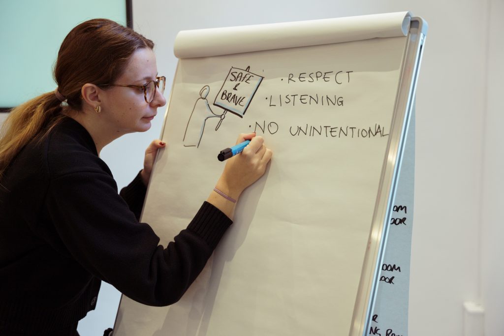 Woman writing "Safe and Brave, respect, listening" on a white board