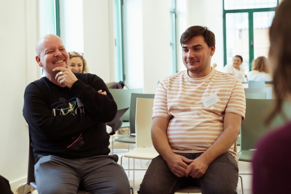 2 men sitting on chairs. One man is smilling