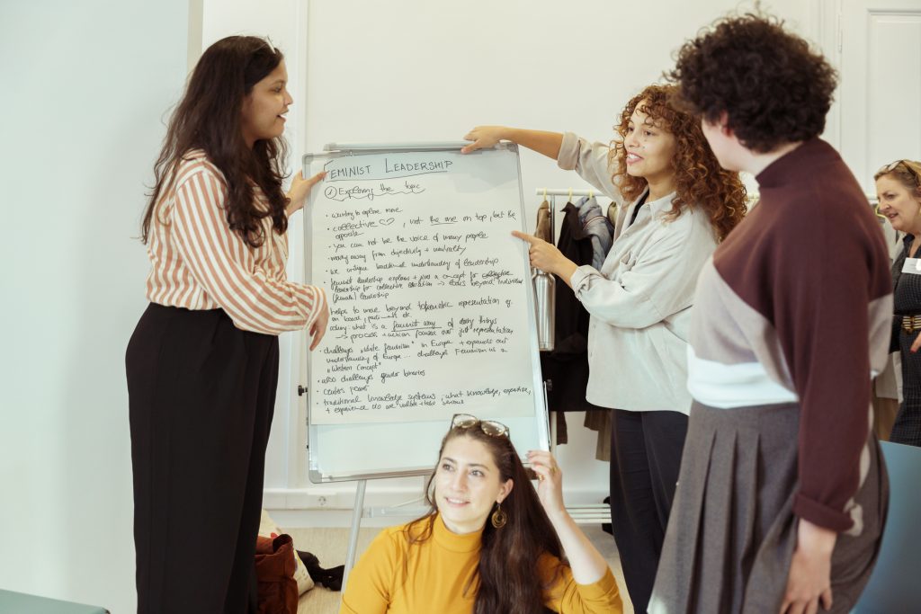 Women discussing together. One woman is showing something written on a whiteboard