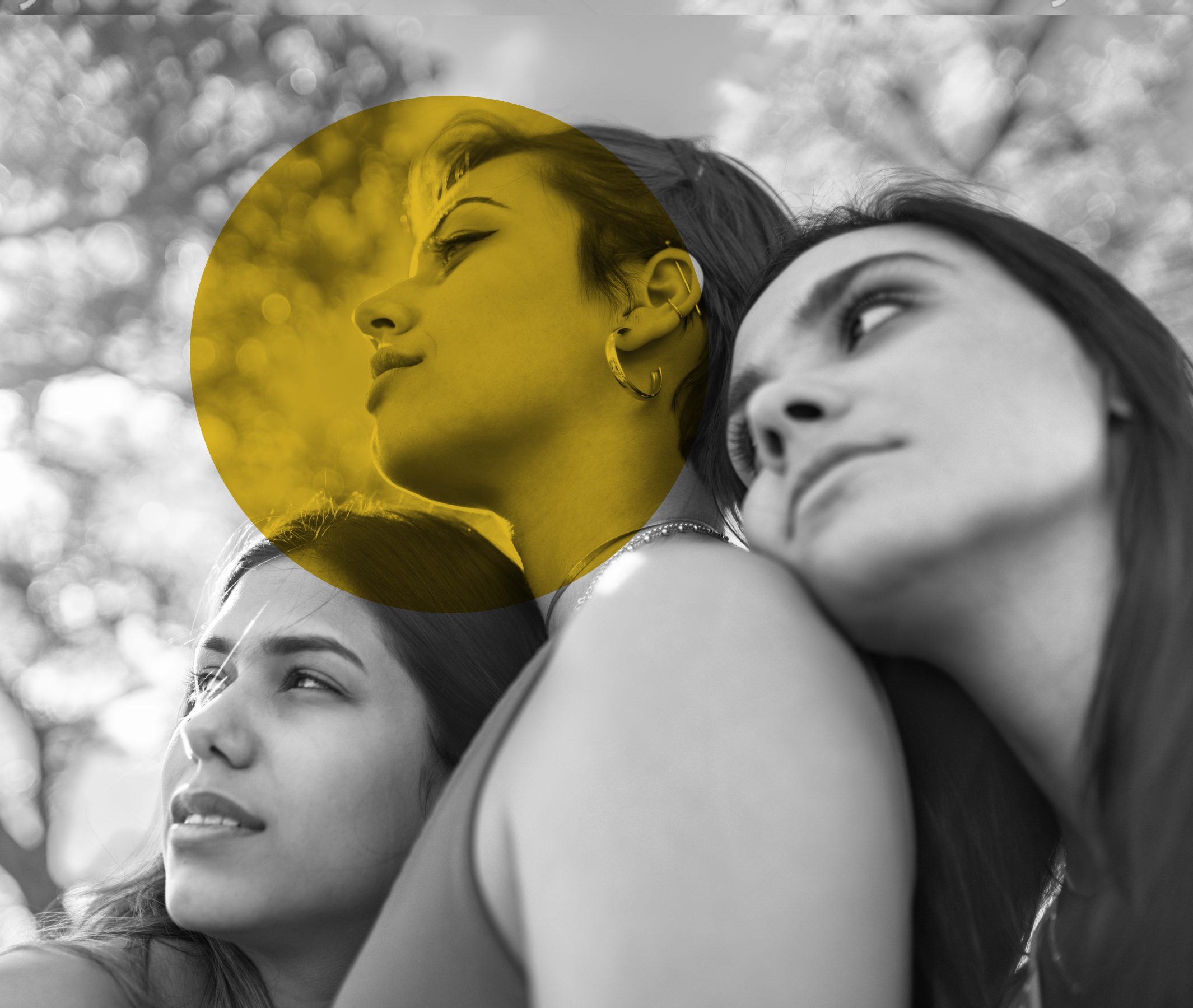Three women cuddling while looking on the left. Photo in black and white with a yellow circle on it.