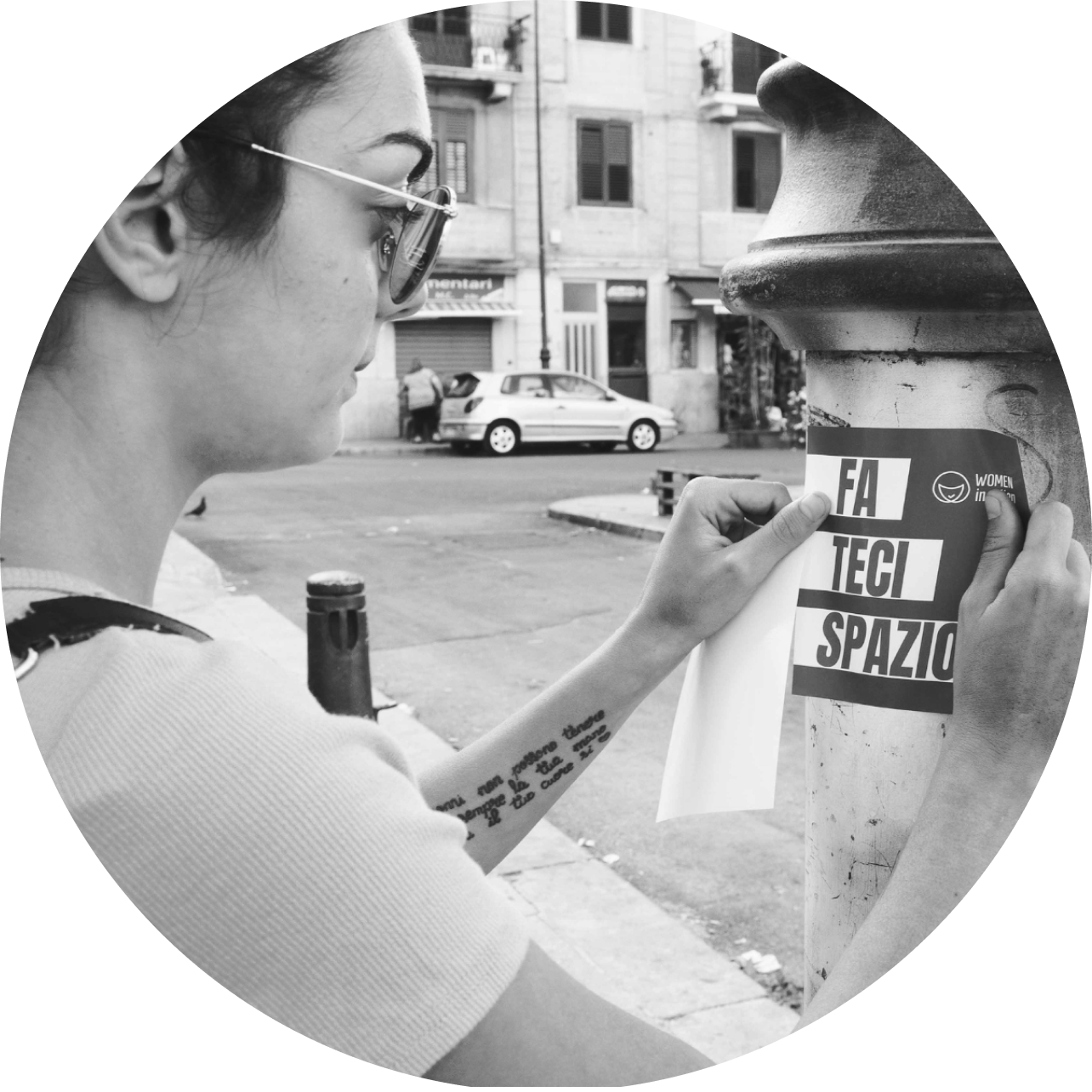 Woman putting a sticker on a light post. Photo in black and white.