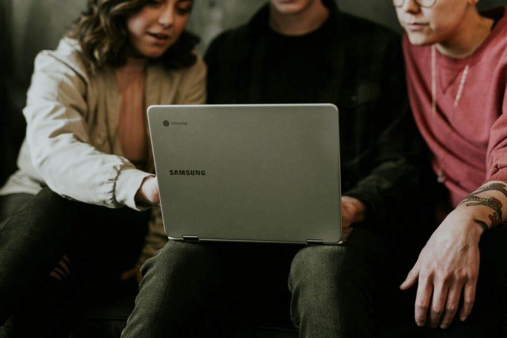 Three people sit together leaning into and looking at the screen of a laptop.