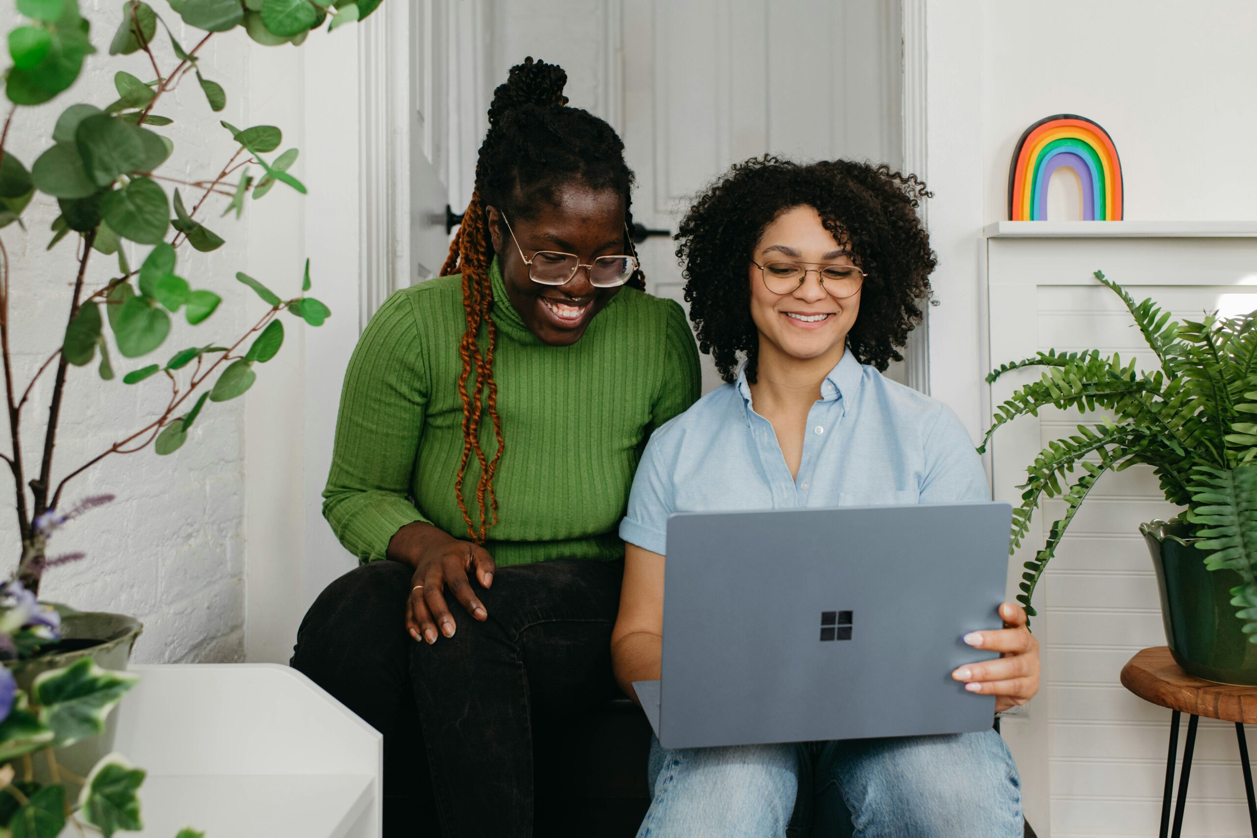 Two women sitting next to each other look at laptop screen while smiling.