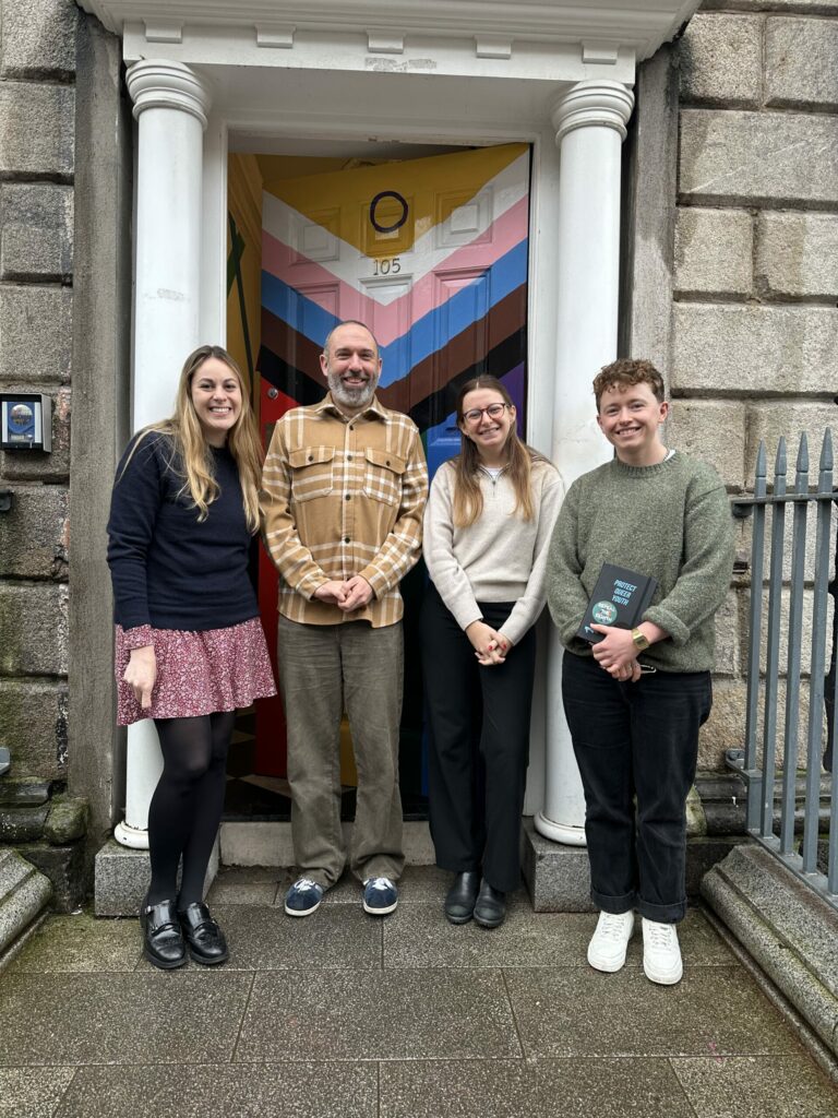 Four people standing in front of a colour door.